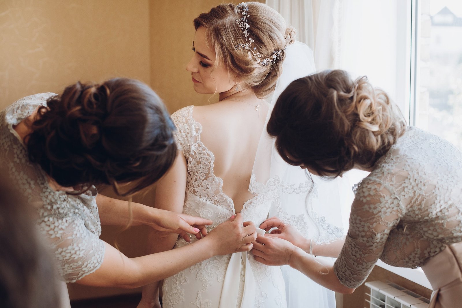 bridesmaids-helping-bride-put-on-lace-wedding-dress.jpg
